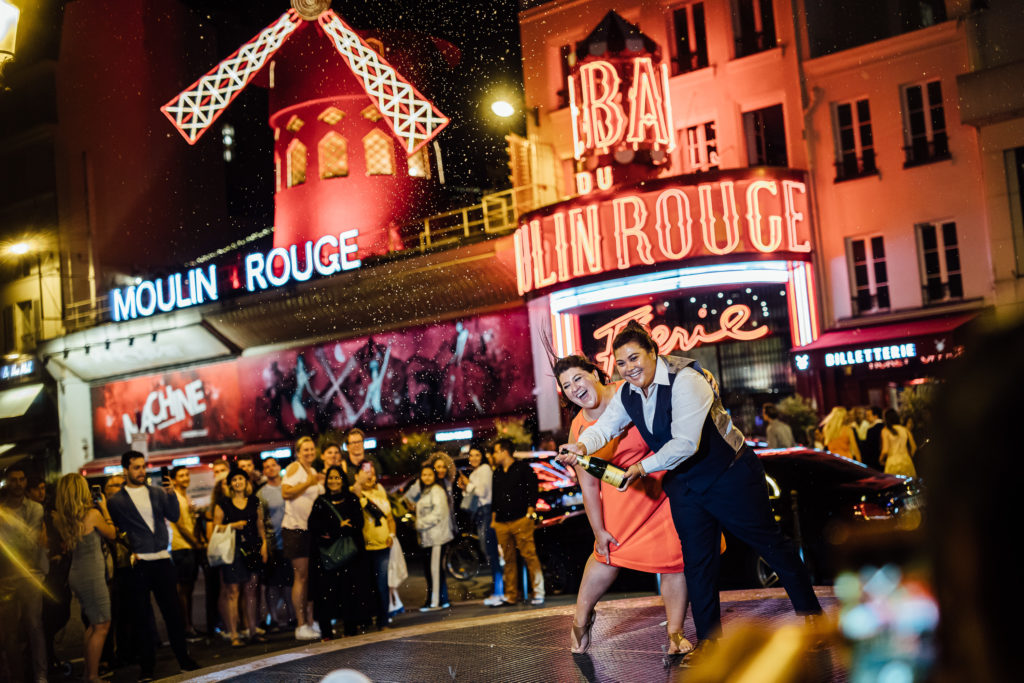 Immerse yourself in the extravagance of the Moulin Rouge, the most popular show in Paris, during an unforgettable evening that includes a gourmet 3-course meal. 
Two women are dancing with champagne, in front of Moulin Rouge, Paris, on July 30th, 2019.